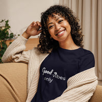 Woman wearing a black sweatshirt with 'Good vibes only' text, sitting on a couch.